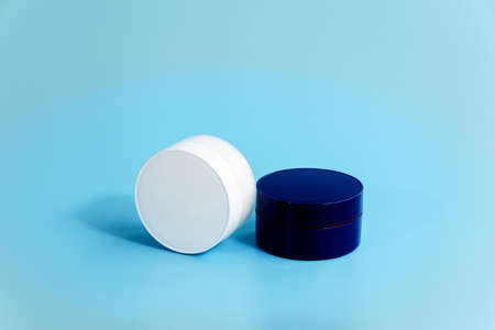Two closed plastic cream jars on light blue background. Blank white and blue cosmetic containers. Day and night facial care concept. Branding of beauty products. Mockup. Copy spaceの写真素材