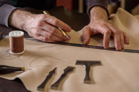 Shoemaker's male hands holding craft knife measuring leather before cutting in workshop. Closeupの写真素材