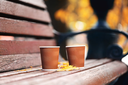 Two paper cups of coffee on wooden bench in autumn park on sunny day. Coffee timeの写真素材