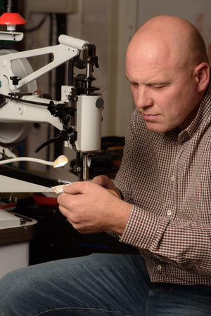 Shoemaker stitching on industrial sewing machine in workshop. Concentrated man setting up sewing...