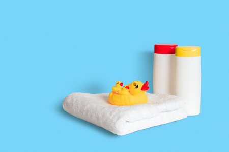 Yellow rubber duck on soft white towel and two plastic white bottles with yellow and red caps on light blue background. Child bath accessories, baby care. copy spaceの写真素材