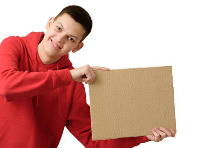 Happy smiling teenage boy dressed red hoodie holding blank brown cardboard banner, isolated on white background. copyspace. close upの写真素材