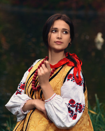 Young woman dressed traditional ukrainian embroidered clothes vyshyvanka. Portrait of beautiful confident girl with long dark hair and brown eyes looking away outdoors. Vintage outfitの写真素材