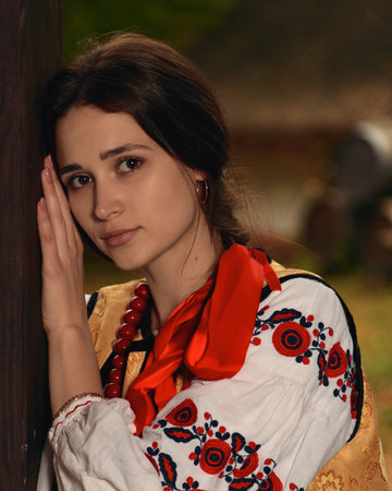 Young pensive woman dressed traditional ukrainian embroidered clothes vyshyvanka. Portrait of beautiful confident girl with long dark hair and brown eyes looking at camera outdoors. Vintage outfitの写真素材