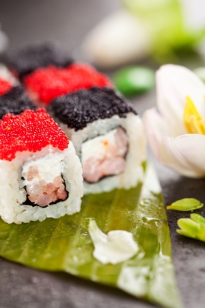 Chess Maki Sushi - Roll with Prawn and Feta Cheese inside. Topped with Black and Red Tobiko (flying fish roe). Served on Banana Leaf with Flowersの写真素材