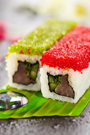 Tobiko Spicy Maki Sushi - Hot Roll Topped with various type of Tobiko (flying fish roe). Tuna, Cucumber and Green Lettuce inside. Served on Banana Leaf with Flowersの写真素材