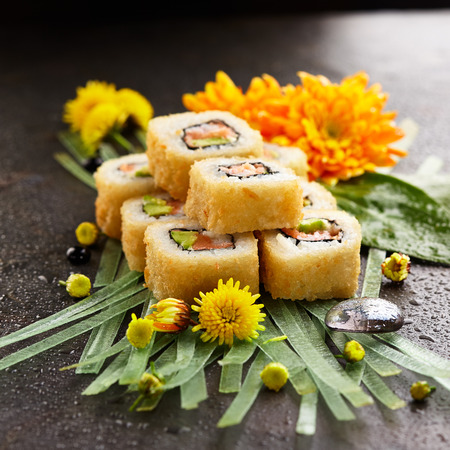 Tempura Maki Sushi - Deep Fried Sushi Roll with Salmon, Crab Meat, Avocado inside. Japanese Sushi Food and Natural Flower Conceptの写真素材