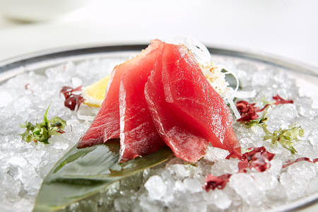 Sashimi with Tuna with  slice of lemon fresh greens on bamboo leaf and in plate full of iceの写真素材