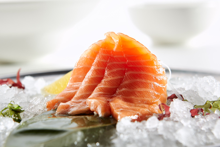 Sashimi with Salmon with slice of lemon fresh greens on bamboo leaf and in plate full of iceの写真素材