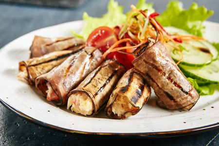 Rustic Fried Stuffed Eggplant Rolls with Cream Cheese Close Up Selective Focus. Grilled Aubergine Decorated with Thin Sliced Cucumbers, Tomatoes and Lettuce Leavesの写真素材