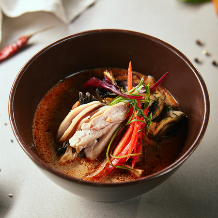 Close-up portrait of tom kha with chicken and mushrooms. Colourful restaurant meal. Tasty dinner presented in round shaped bowl. Japanese food concept on blurred backgroundの写真素材