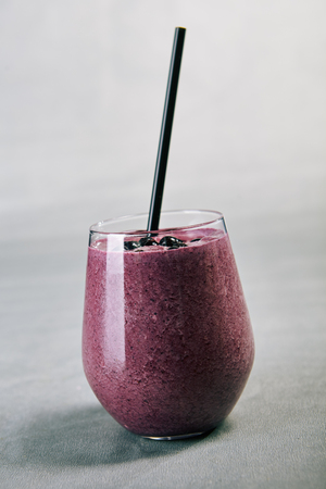 Close-up picture of glass of smoothy with juicy bilberry banana and tasty yogurt. Purple cooling beverage. Summer drink concept. Isolated on grey backgroundの写真素材