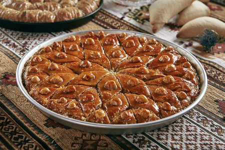 Beautiful Serving Homemade Baklava in a Round Metal Tray on Vintage Traditional Tablecloth. Sweet Turkish Style Brown Glazed Pastries Baklawa with Walnut, Nuts, Sugar, Pistachio and Honey Close Upの写真素材