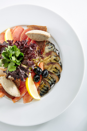 Elegant Restaurant Plate with Fish Delicacies Top View. Smoked Butter Fish, Salmon, Perch, Marinated Dorado, Forshmak with Lemon, Olives, Quail Egg, Greens and Bread Crispsの写真素材