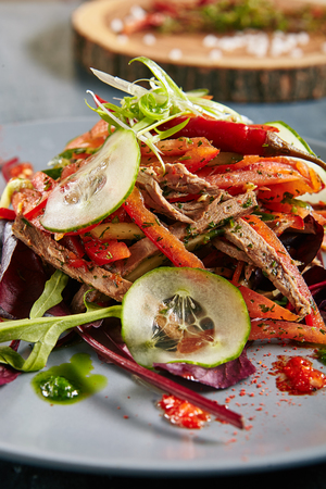 Spicy Salad with Beef, Greens, Bulgarian Pepper, Tomato, Cucumber, Sesame, Garlic and Chili Close Up. Russian Winter Salad with Meat Strips, Dried Spices and Vegetablesの写真素材