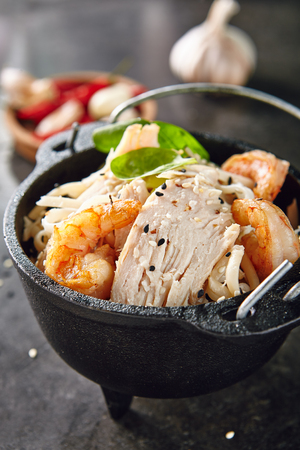 Noodles with Shrimps, Chicken, in Metal Bowler with Sesame Seeds on Natural Dark Stone Background. Meat Dish with Greens, Lettuce and Spices in Oriental Restaurantの写真素材