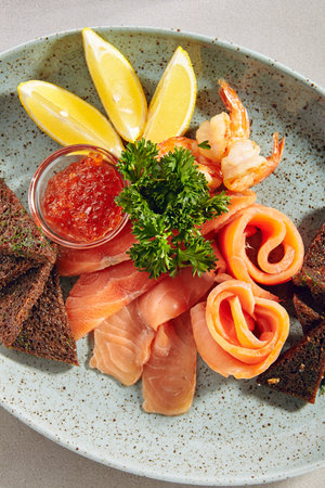Fish platter with light-salted salmon, smoked salmon, red caviar and Borodino triangular black bread toast with green parsley close up. Delicacy fresh seafood sashimi dish with sliced troutの写真素材
