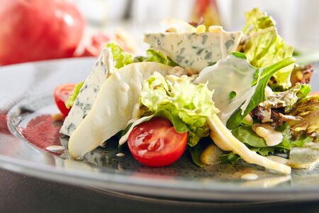 Salad with sliced pears, gorgonzola cheese, greens and pine nuts close up. Fruit salat with Italian blue cheese, tomatoes, green lettuce leaves, thin slices of pear and white sauceの写真素材
