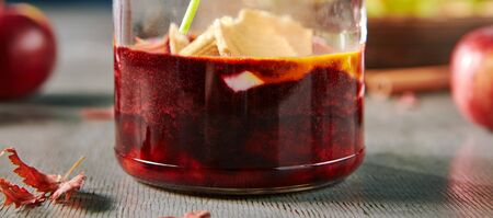 Autumn dessert with chokeberry jam in glass jar and baked apple on skewer. Red fruit autumnal marmalade or black rowan confiture close up with selective focusの写真素材