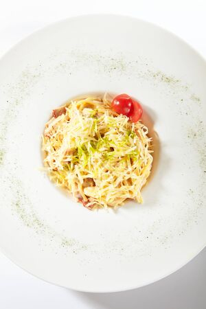 Delicious spaghetti carbonara with grated parmesan cheese isolated. Exquisite white restaurant plate of classic italian egg pasta with fried bacon and fresh tomatoes top viewの写真素材