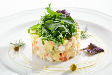 Classic Olivier salad or Russian salad with chicken fillet, quail eggs, pickles, greens and peas on white plate isolated. Traditional Christmas salat or Stolichny salad on a white plate in restaurant closeupの写真素材