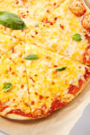 Pizza margarita or margherita with cherry tomatoes, tomato sauce, green basil and mozzarella cheese isolated. Traditional italian whole yeasted flatbread on wooden plate with kraft paper closeupの写真素材