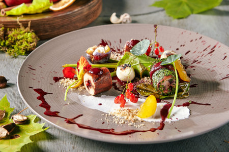 Exquisite serving vintage plate of turkey meat roulade or meatloaf with aronia sauce, barberry berries, plums and cheese. Autumn restaurant menu decorated with edible flowers and nasturtium leavesの写真素材
