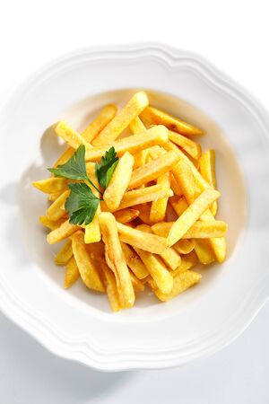 Top view of fries or french fries on white restaurant plate isolated. Sweet potato finger chips, french-fried potatoes, delicious fast food with salt and a leaf of parsley topviewの写真素材