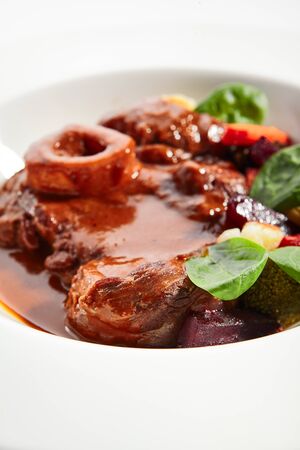 Ossobuco dish closeup. Veal shank with steamed veggies isolated on white background. Beef with demi glace sauce. Italian traditional cuisine. Served and plated delicious food compositionの写真素材
