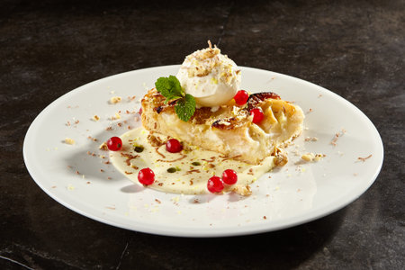 Apple pie slice with ice cream scoop side view. Delicious fruit cake with mint sauce and leaves. Baked tart with vanilla gelato and berries on white plate. Sweet dessert on black tableの写真素材