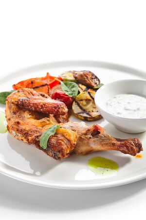 Tapaka or tabaka chicken with grilled vegetables on white restaurant plate isolated. Traditional Georgian pan-fried tobacco chicken with barbecue zucchini, eggplant, pepper, tomato and onion side viewの写真素材