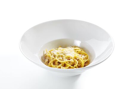 Italian spaghetti alla carbonara with grated parmesan, hard pecorino romano cheese, fried bacon, guanciale or pancetta, egg sause and black pepper on white restaurant plate isolated side viewの写真素材