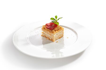 Square piece of traditional russian honey cake medovik with gentle sour cream on white restaurant plate isolated. Slice of layered sponge caramel tart with fresh strawberries and mint closeupの写真素材