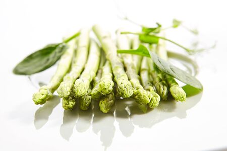 Fresh young asparagus stalks and spinach leaves isolated on white background. Raw garden asparagus or Asparagus officinalis, green vegetable closeupの写真素材