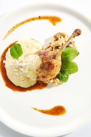 Duck leg confit with pearl barley on restaurant plate isolated. Top view of cooked poultry leg quarter with orange sauce, fresh spinach leaves and cheese closeupの写真素材