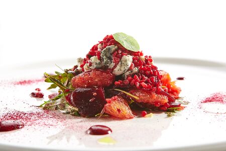 Baked beet salad with citrus fruits and stracciatella on restaurant plate isolated. Red salat with sliced beets, grapefruit, pomegranate, cheese ice cream closeupの写真素材