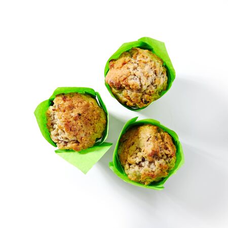 Three muffins or cupcakes in green paper isolated on white background. Traditional American bakery chocolate dessert with nuts, raisins and candied fruits for children menu closeupの写真素材