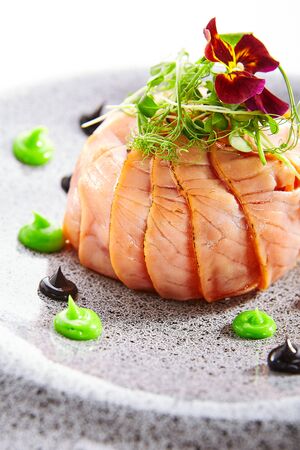 Salmon olivier salad with sauces. Sliced fish dish with greenery. Tasty seafood decorated with violet flower. Haute cuisine on plate. Restaurant meal, elegant food compositionの写真素材