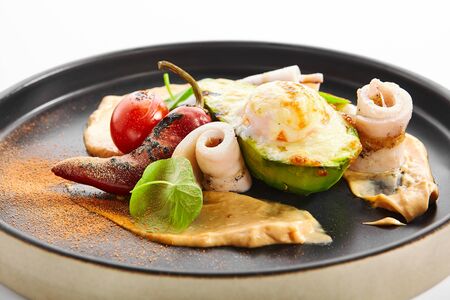 Grilled squid with avocado and egg. Roasted seafood closeup view. Delicious meal with greenery, pepper and creamy sauce. Haute cuisine, cooking process. Food ingredients, culinary menuの写真素材
