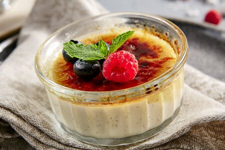 Classic creme brulee in glass bowl. Appetizing ice cream close up. Delicious dessert with blueberry and raspberry, Sugary meal with caramel, mint and berries decoration. Restaurant sweet foodの写真素材