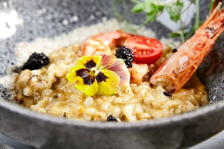 Risotto with seafood in gray bowl . Italian rice porridge with shrimps close up. Traditional food with violet flowers, black caviar, tomato and greenery decoration. Served delicatessenの写真素材