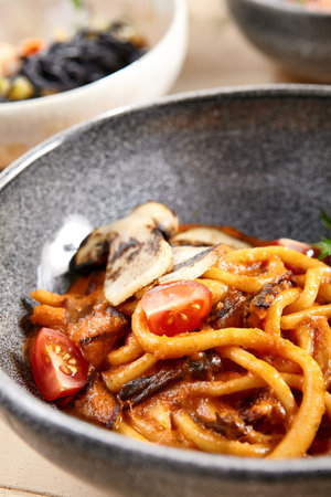Pichi with mushrooms and creamy tomato allione in gray bowl. Pasta with vegetables close up. Delicatessen, served restaurant meal, tasty noodles with tomato and greenery leaves decorationsの写真素材