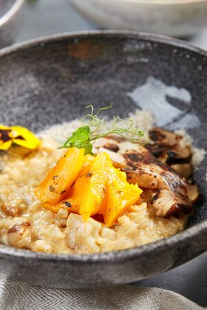Risotto with white mushrooms and pumpkin in gray bowl. Italian rice porridge close up. Delicious traditional food with violet flowers and greenery decoration. Served restaurant meal, delicatessenの写真素材