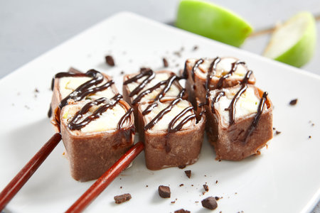 Chocolate pancake in ceramic white plate. Roll with mascarpone cheese, cream cheese, kiwi, coconut,...