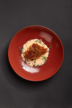 Cod piece with sauce in red deep plate. Fish cooked in tomato crumbs top view. Seafood dish in bowl...