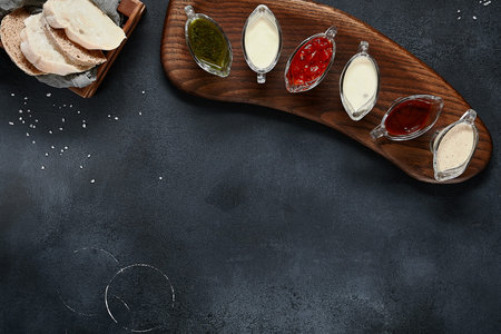 Assortment sauce on wooden board. Black slate table top view. Bread and Pepper overhead. Copy space