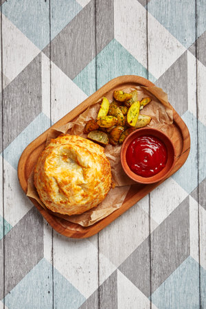 Roasted round cheese loaf and fried potatoes. Restaurant dish portion. Fast food serving with tomato sauce on wooden tray side view. Cafe quick meal close up. Course helping side shotの写真素材
