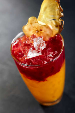 Cuba sling cocktail on dark stone background. Black slate table. Party cocktail with pineapple and berry syrupの写真素材