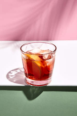 Negroni cocktail over pink background. Drink in rox glass in daylight with palm leaf hard shadow. Summer, tropical, fresh drink concept.の写真素材