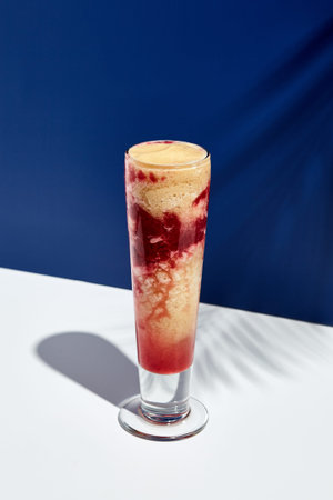 Raspberry and banana smoothie over white and blue background. Palm leaf with sunshine and hard...